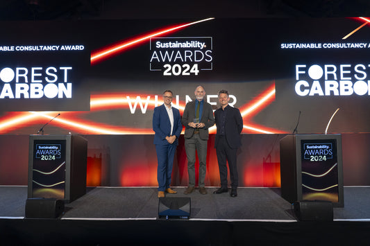 Three people stand on stage at the Sustainability Awards 2024, where "Forest Carbon" is displayed prominently in the background, celebrating Forest Carbon's win of the Sustainable Consultancy Award