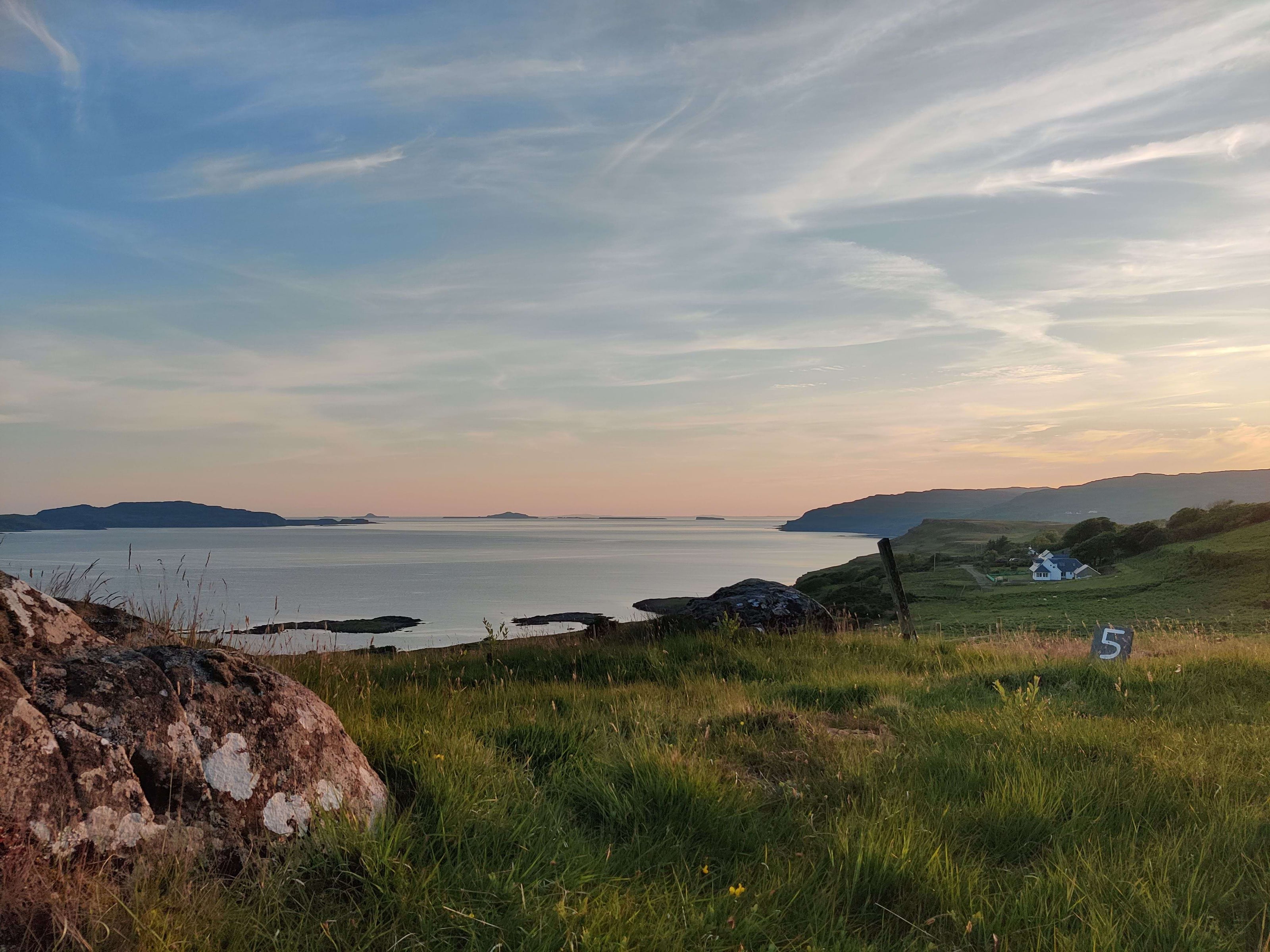 Scenic view of a coastal landscape with grassy field, rocks, and water under a blue sky.