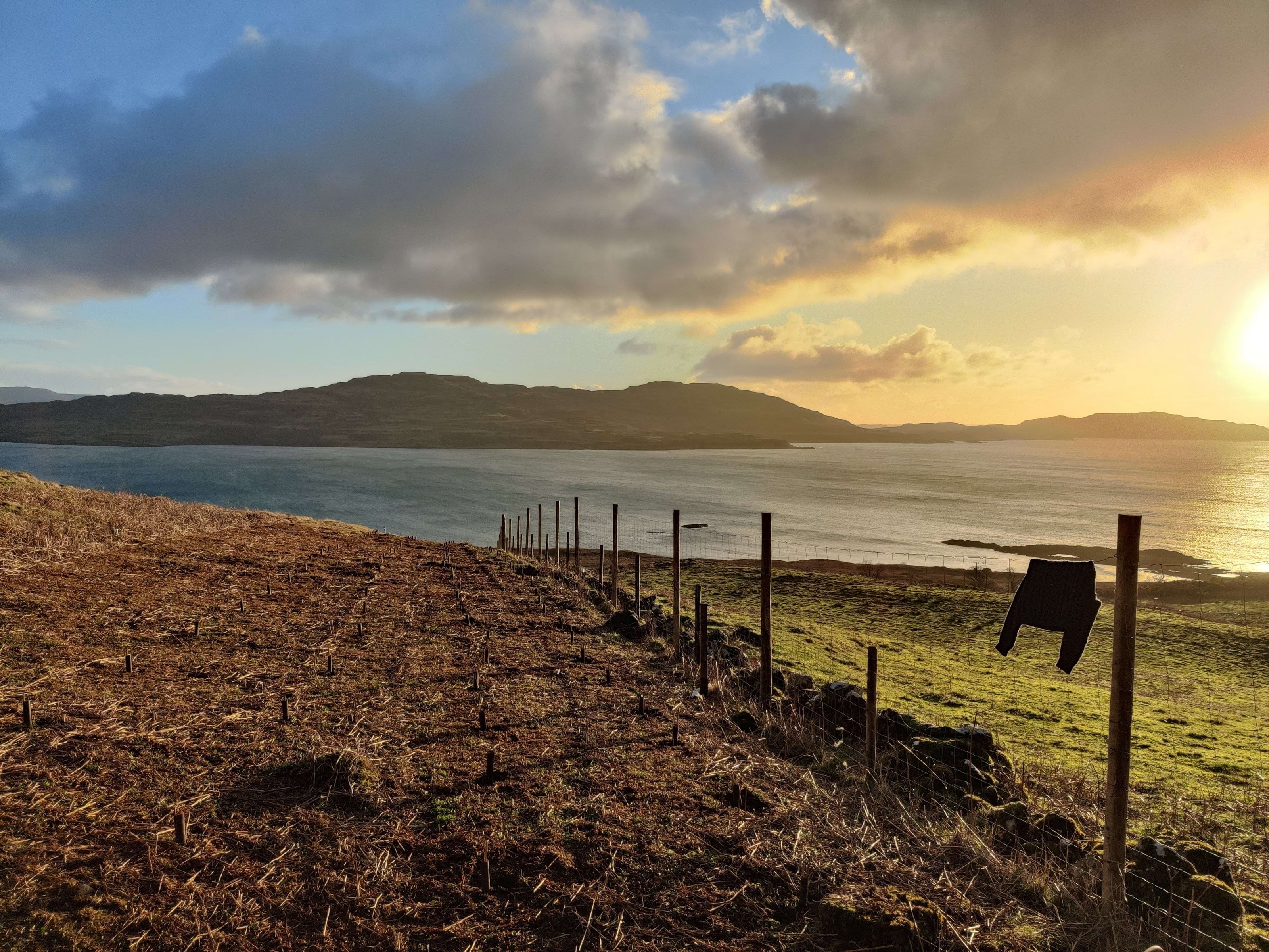 Scenic view of a coastal landscape with a fence and mountains in the background.