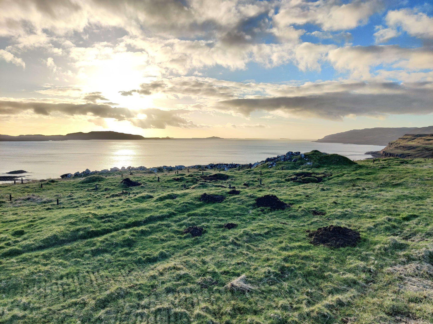 Scenic view of a grassy field with a body of water and distant land under a cloudy sky.