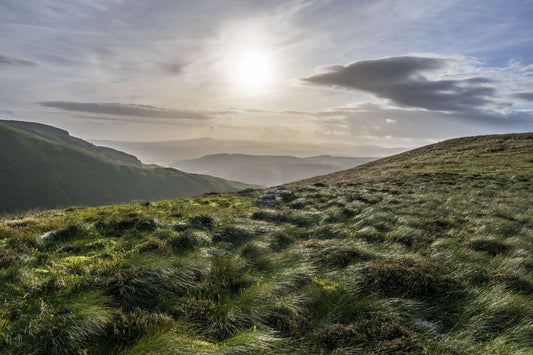 A scenic view of a grassy hillside with gently rolling hills in the background.